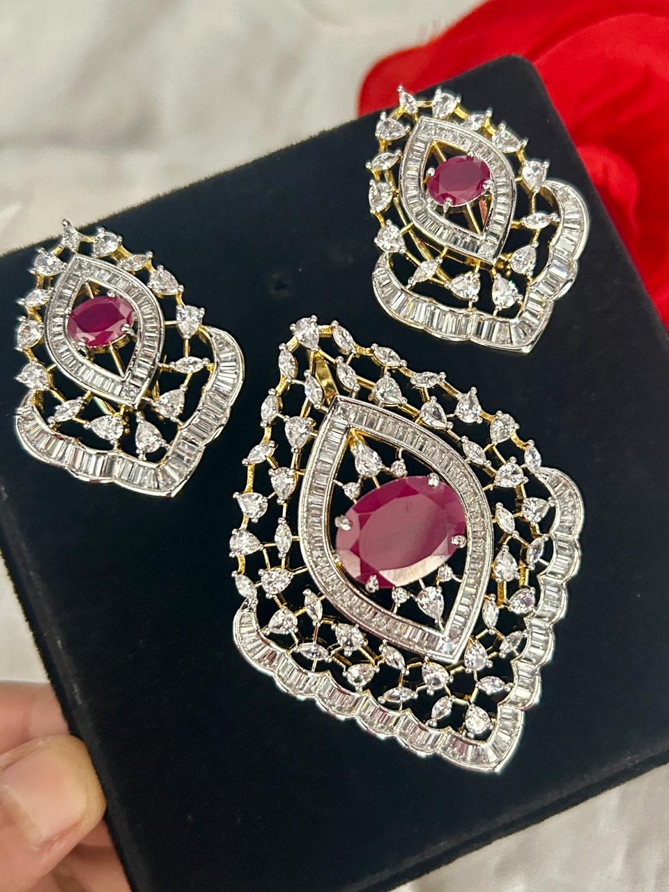 Ornate earrings with red gemstones and gold accents on a black stand.