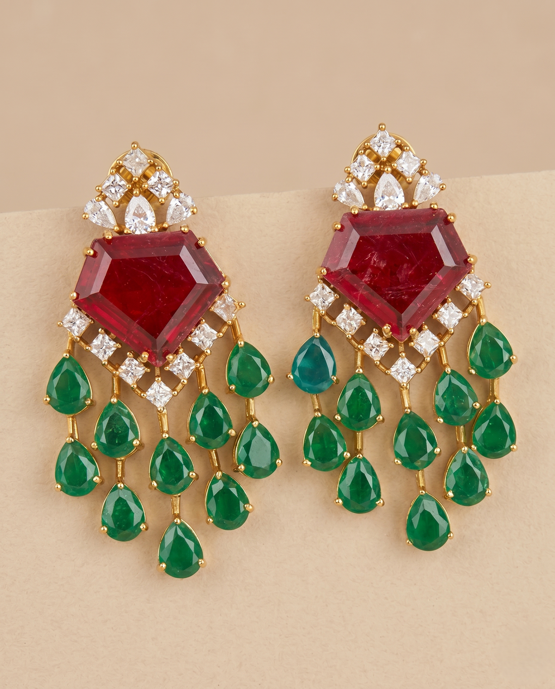 Ornate earrings with red gemstones and green teardrop-shaped stones on a beige background
