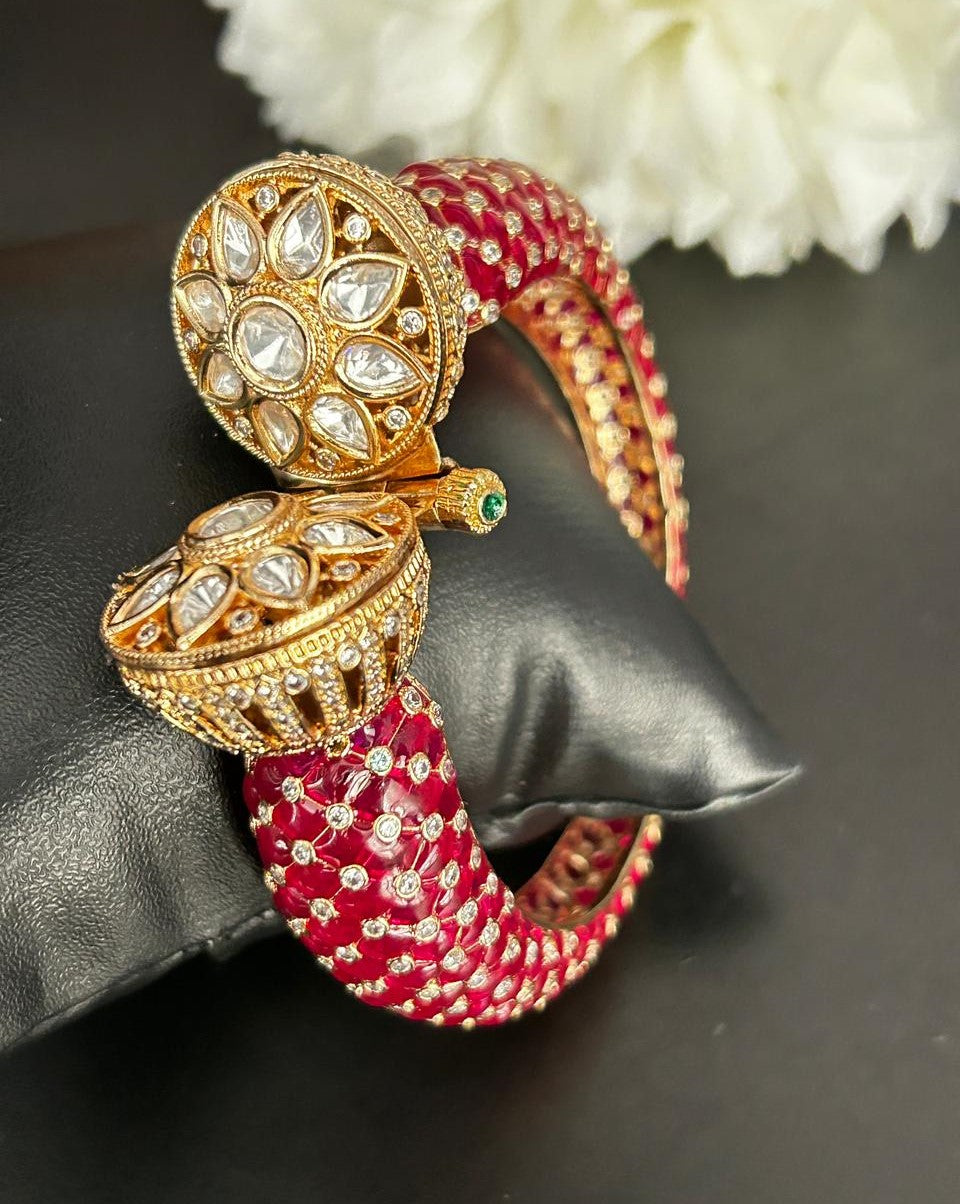 Ornate gold and red earrings on a dark surface with white flowers in the background