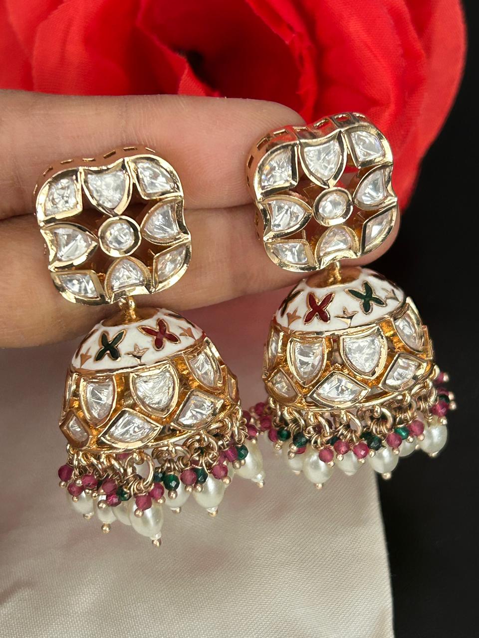 Ornate gold earrings with gemstones held by a hand against a red fabric background
