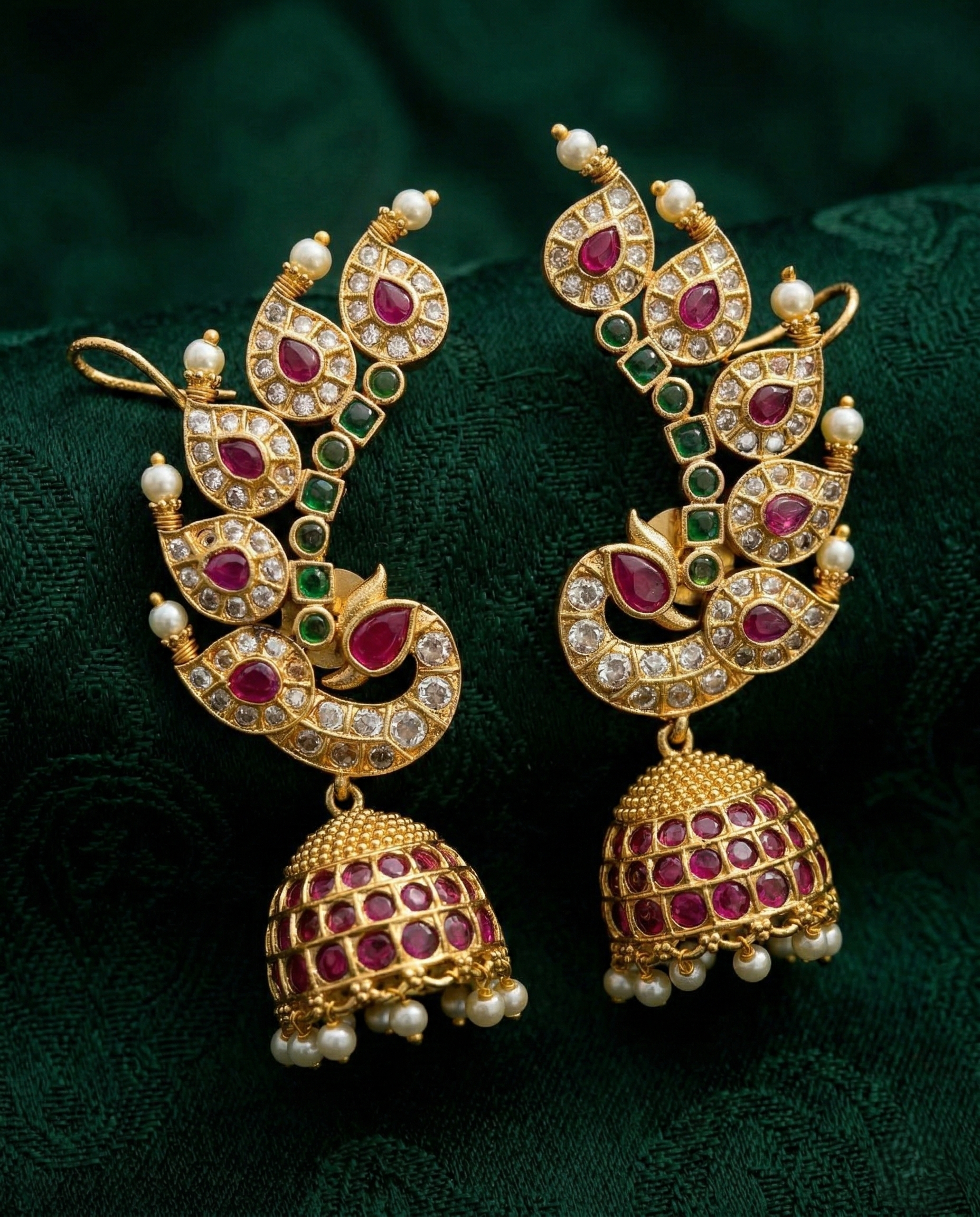 Ornate gold earrings with gemstones on a dark green fabric background