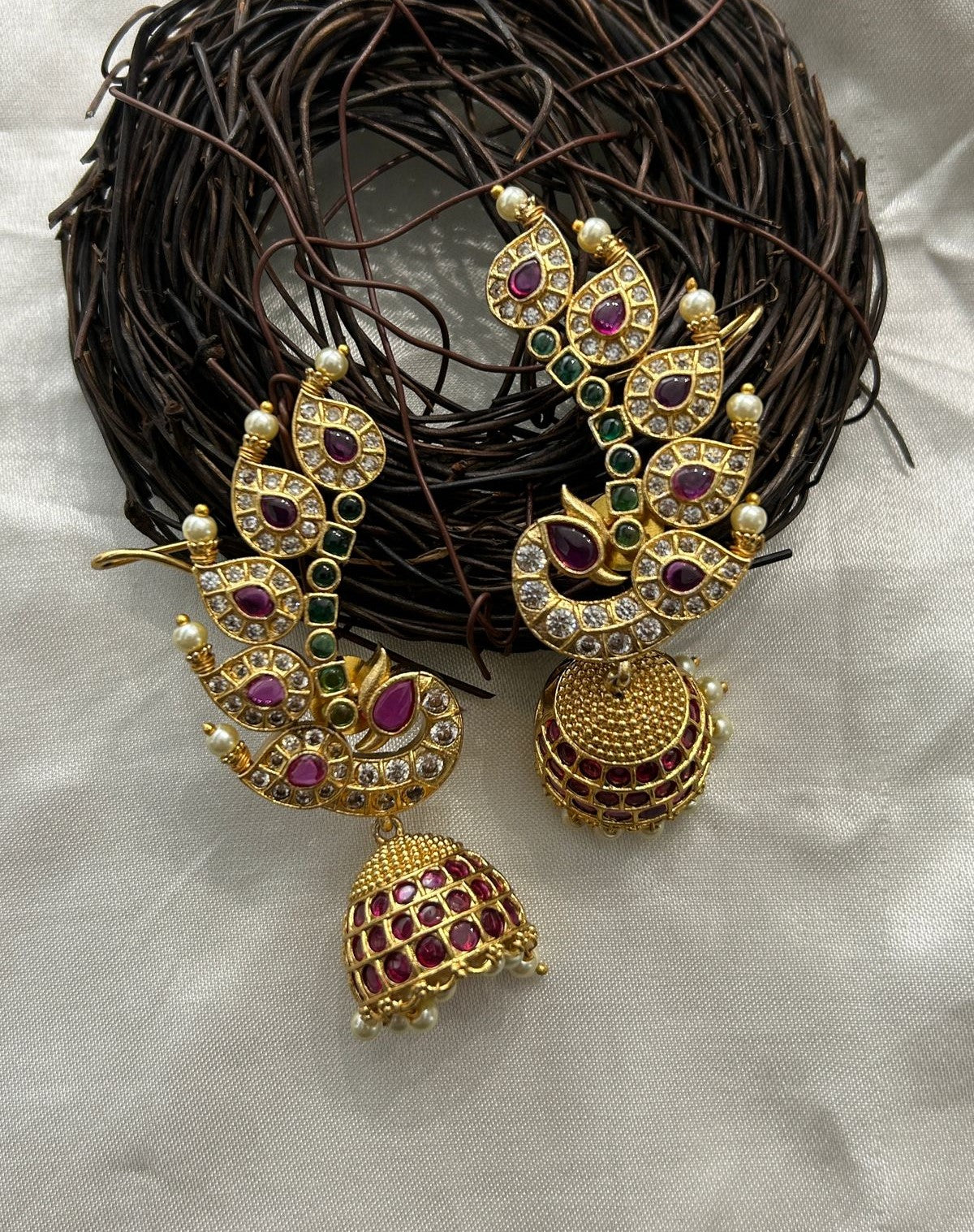 Ornate gold earrings with gemstones on a textured surface