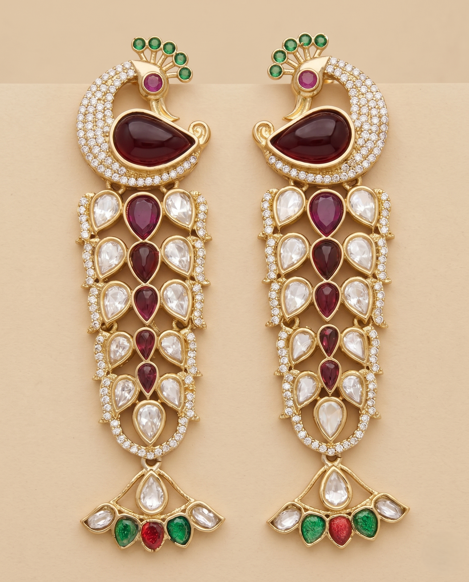 Ornate gold earrings with red, green, and white stones on a beige background