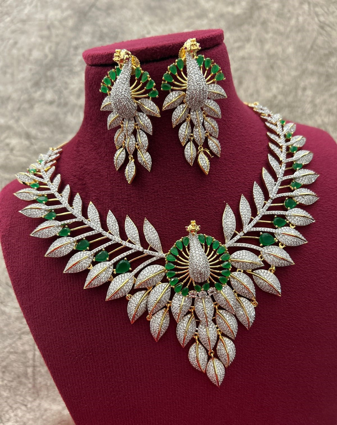 Ornate necklace and earrings set on a red stand with a neutral background