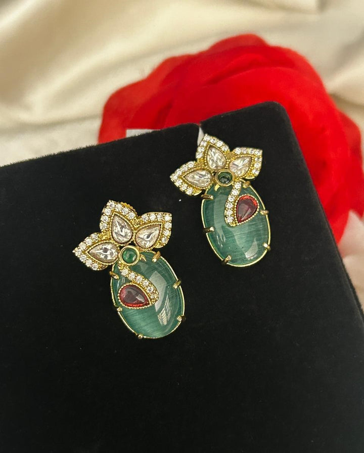 Pair of decorative earrings on a black stand with a red flower in the background