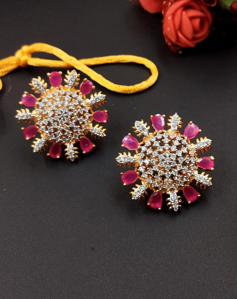 Pair of decorative earrings with pink gemstones on a dark surface.