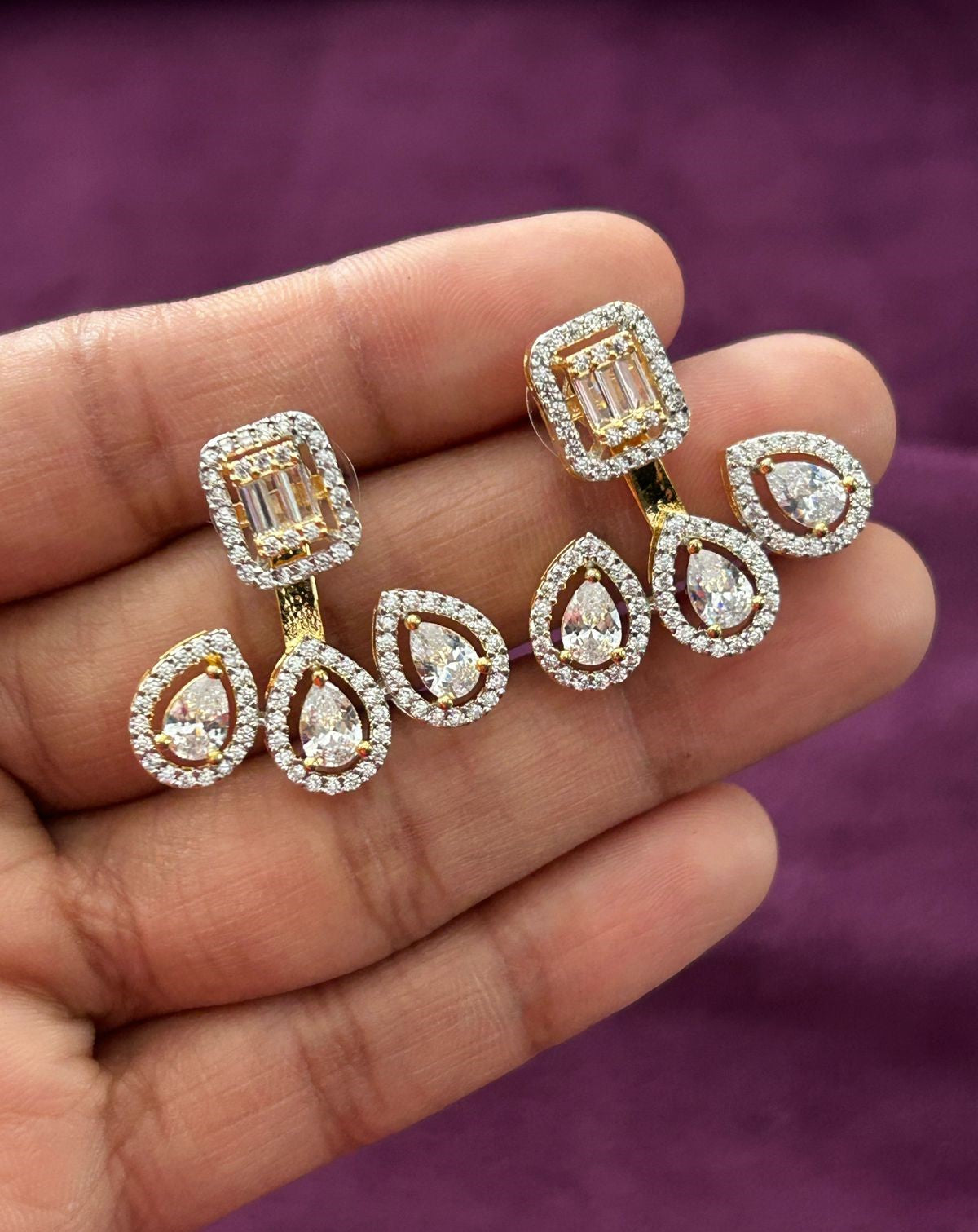 Pair of diamond earrings held in a hand against a purple background