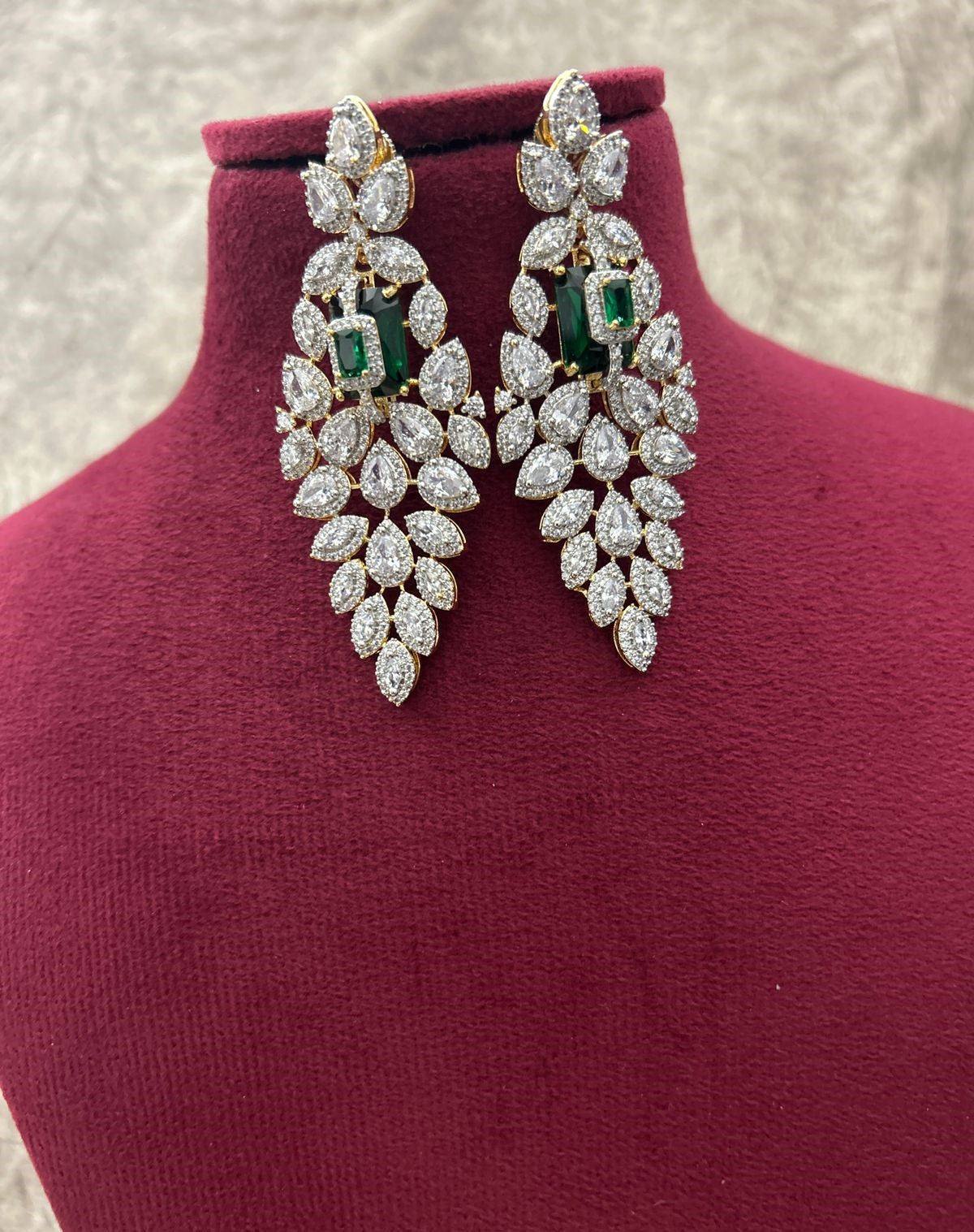 Pair of diamond earrings with green gemstones on a mannequin bust.