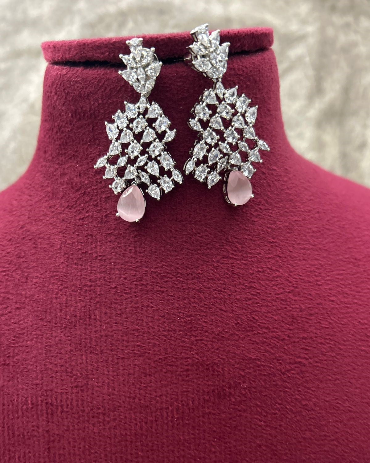 Pair of diamond earrings with pink gemstones on a mannequin bust.