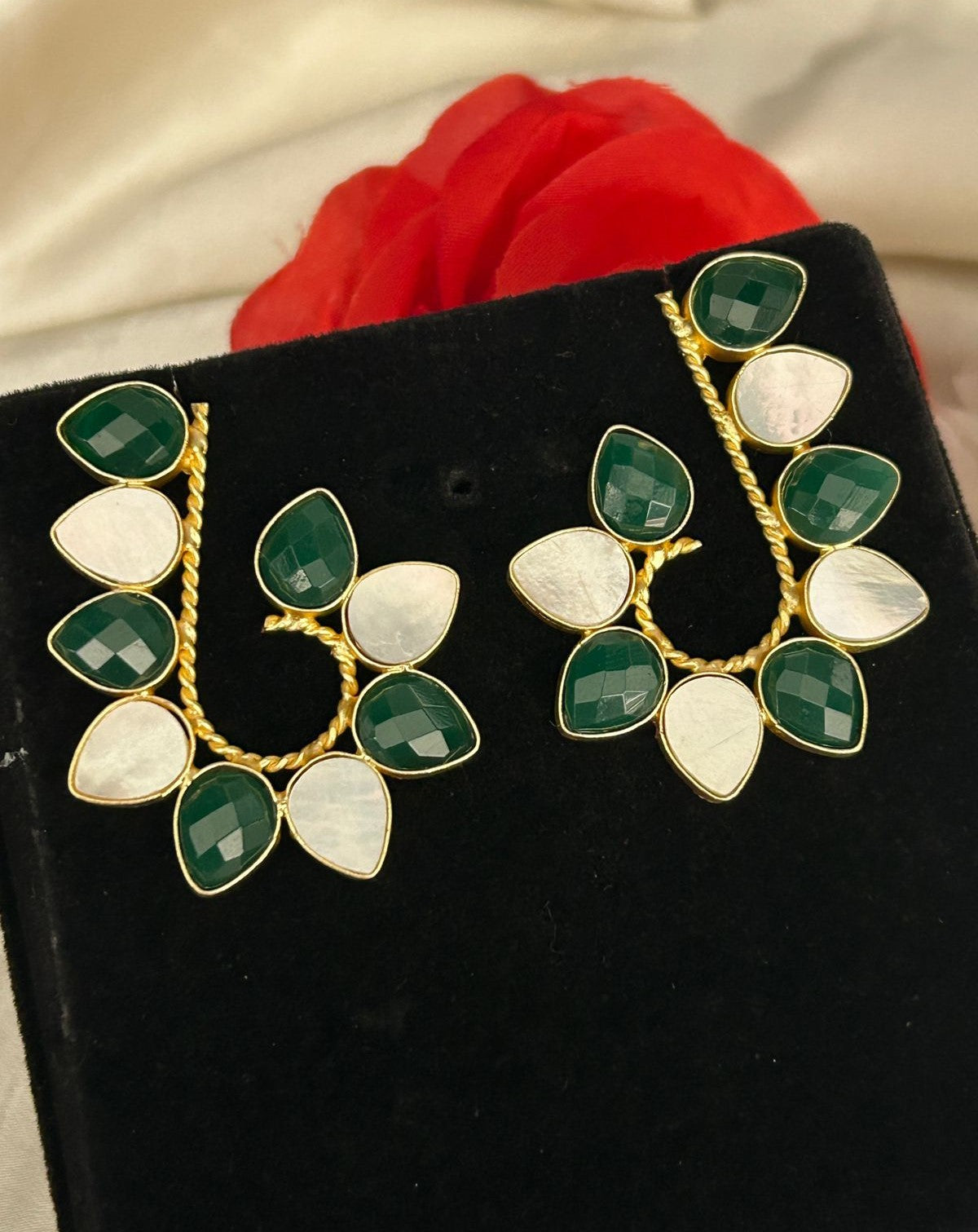 Pair of earrings with green and white stones on a black stand.