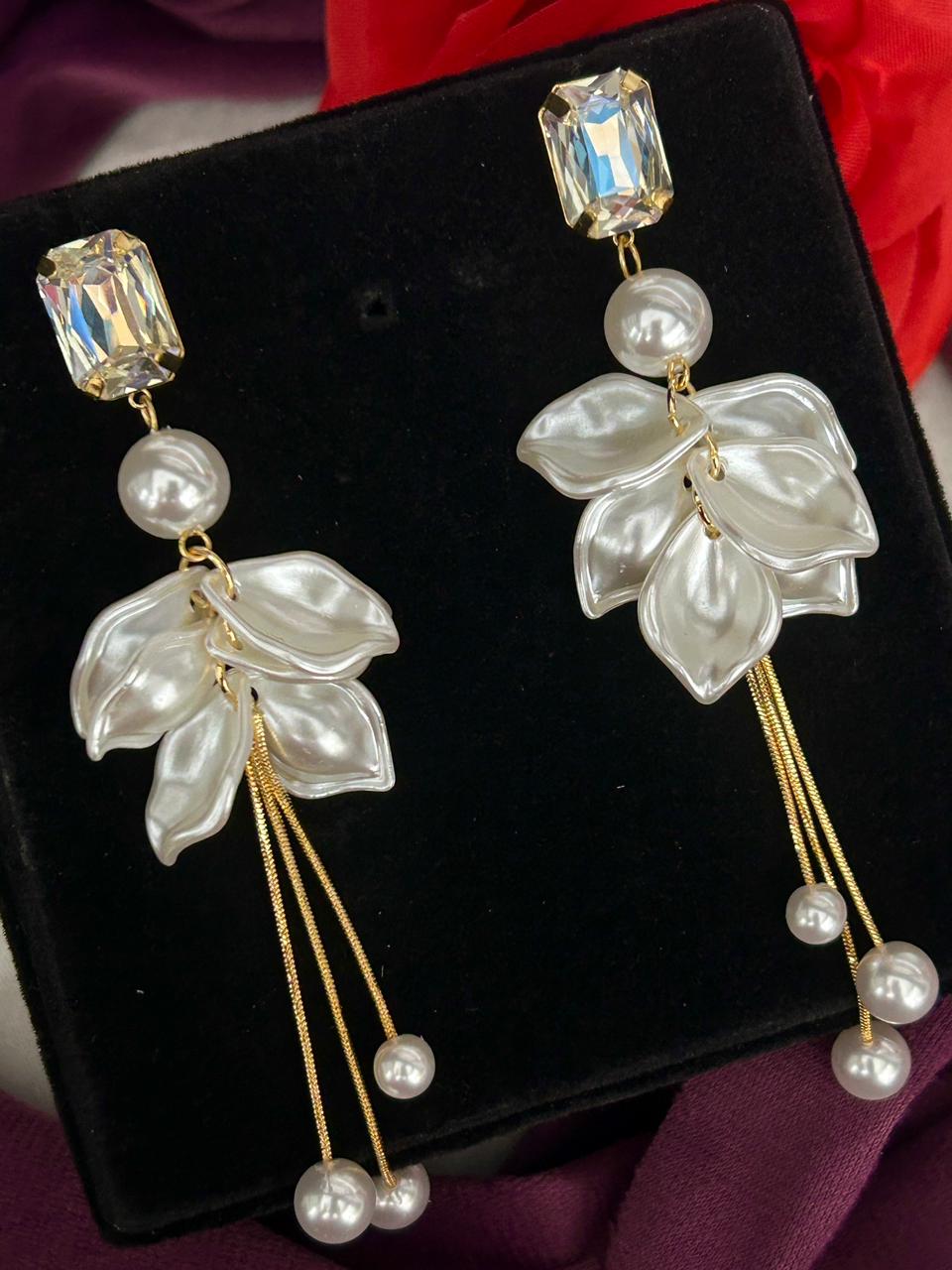 Pair of earrings with leaf and pearl designs on a black stand.