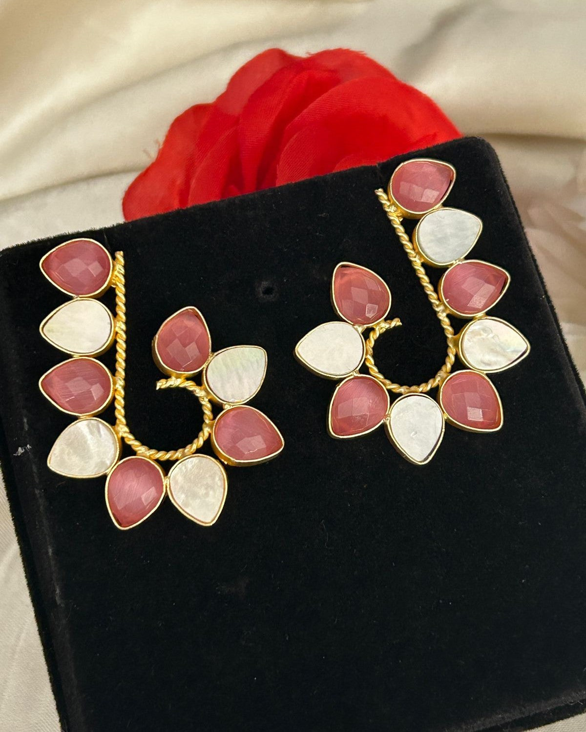 Pair of earrings with pink and white stones on a black stand with red fabric in the background