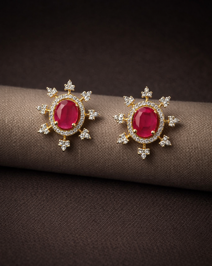 Pair of earrings with red gemstones and gold accents on a brown fabric background