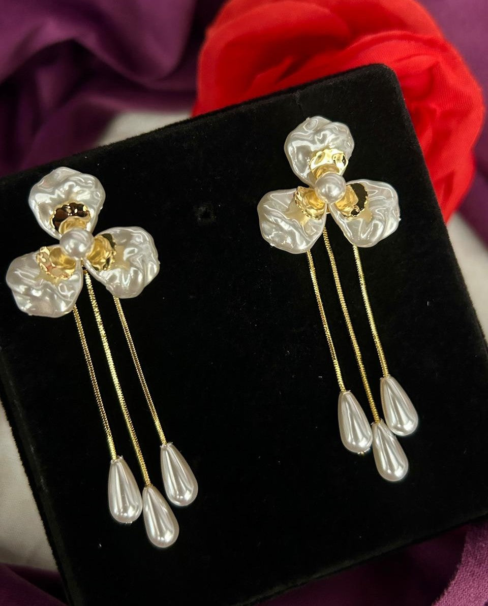 Pair of floral earrings with pearl-like stones on a black stand with red fabric in the background