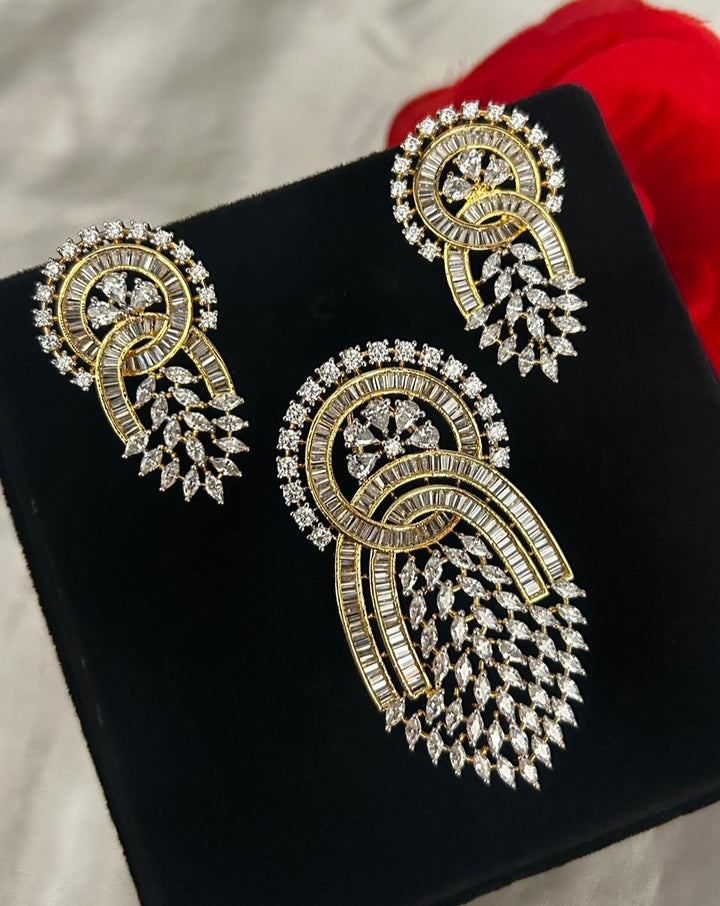 Pair of gold and diamond earrings on a black surface with a red fabric background