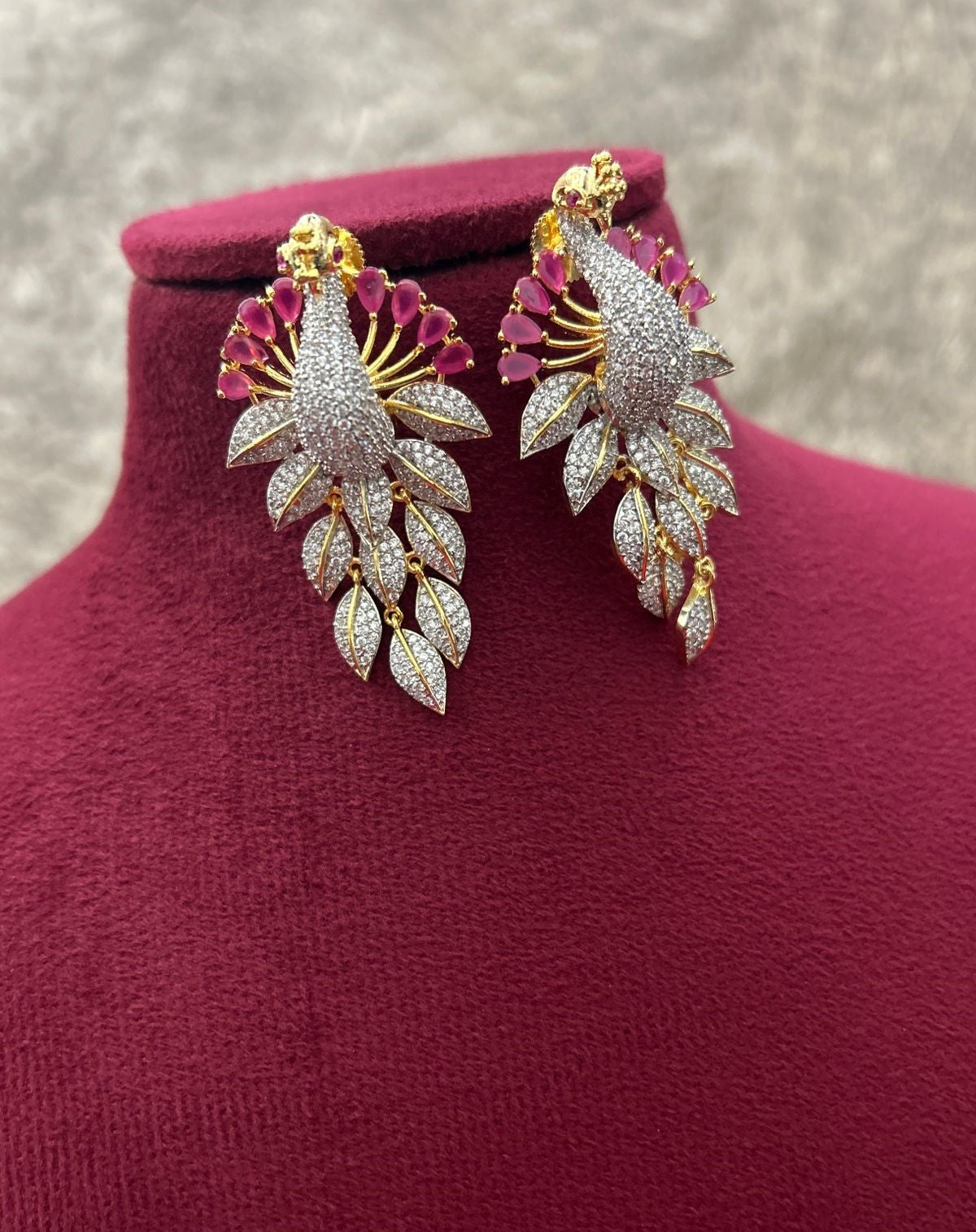 Pair of gold and diamond earrings on a red cushion with a blurred background
