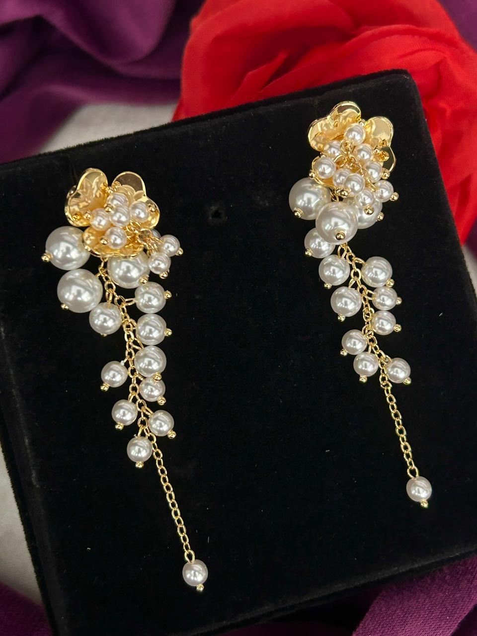 Pair of gold and pearl earrings on a black velvet stand with red fabric in the background.