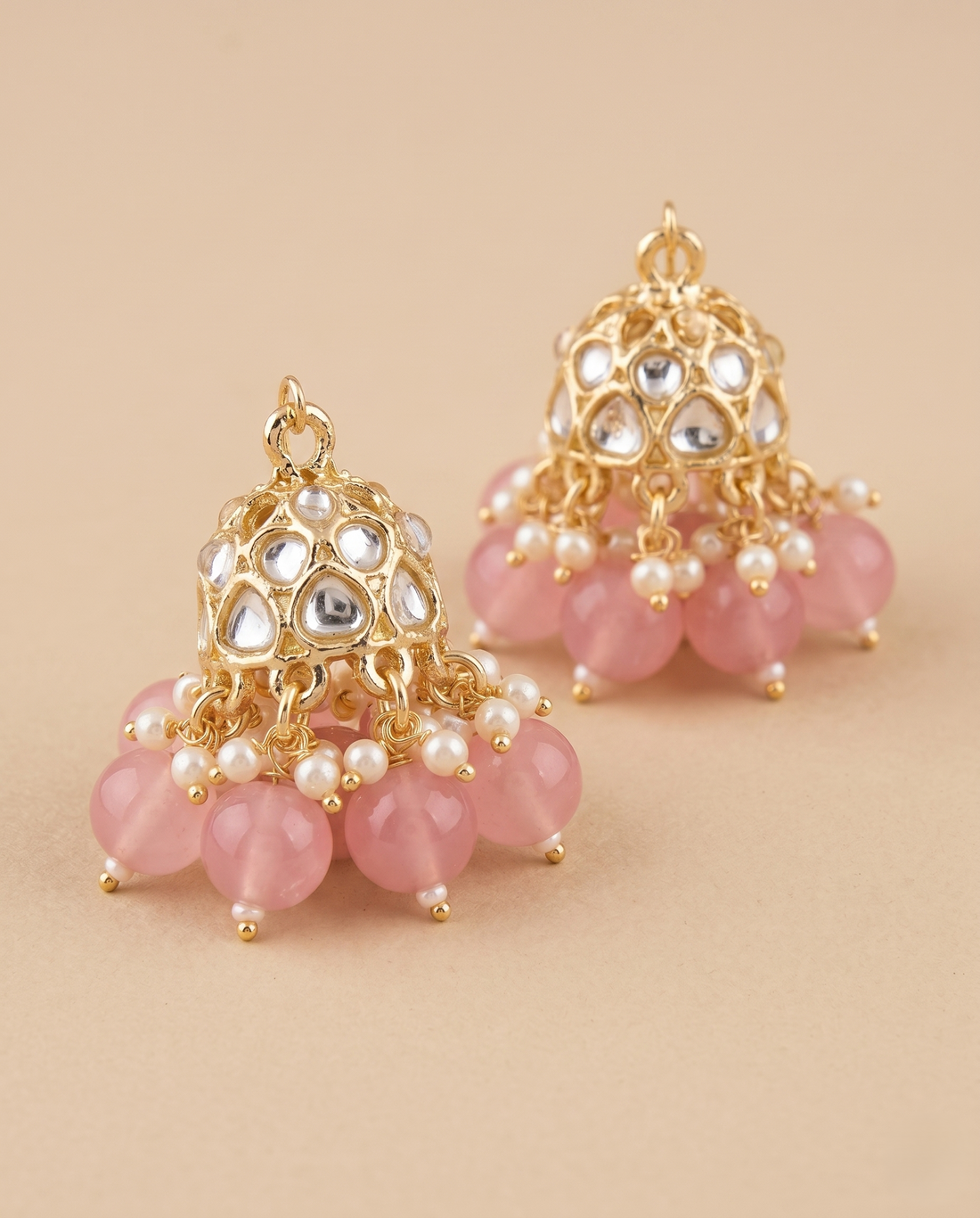 Pair of gold and pink beaded earrings on a beige background
