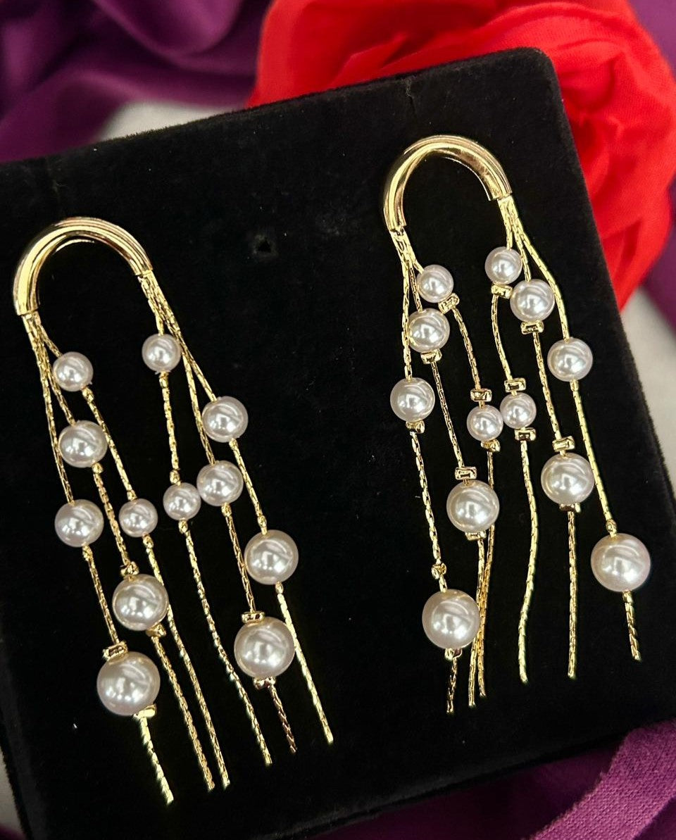 Pair of gold earrings with pearl beads on a black velvet surface.