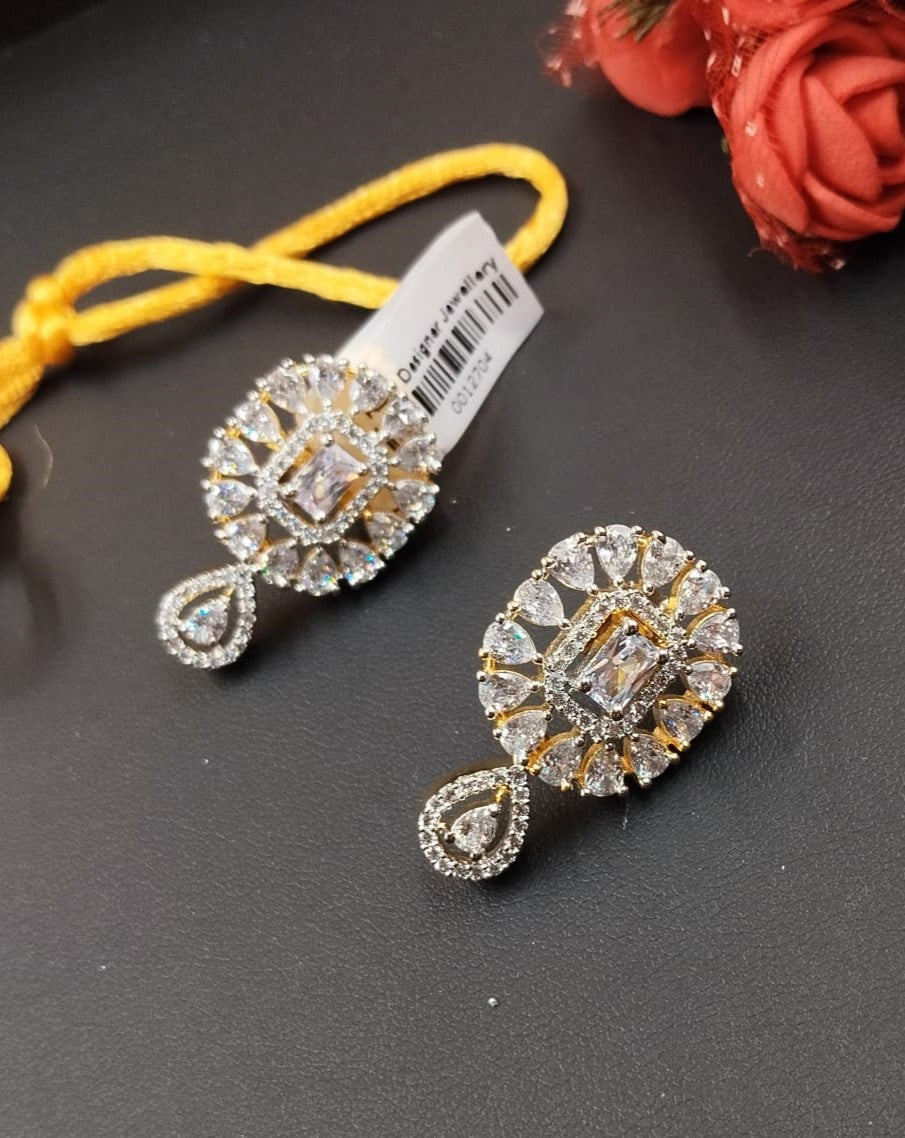 Pair of ornate earrings with a yellow string and red flowers in the background on a dark surface.