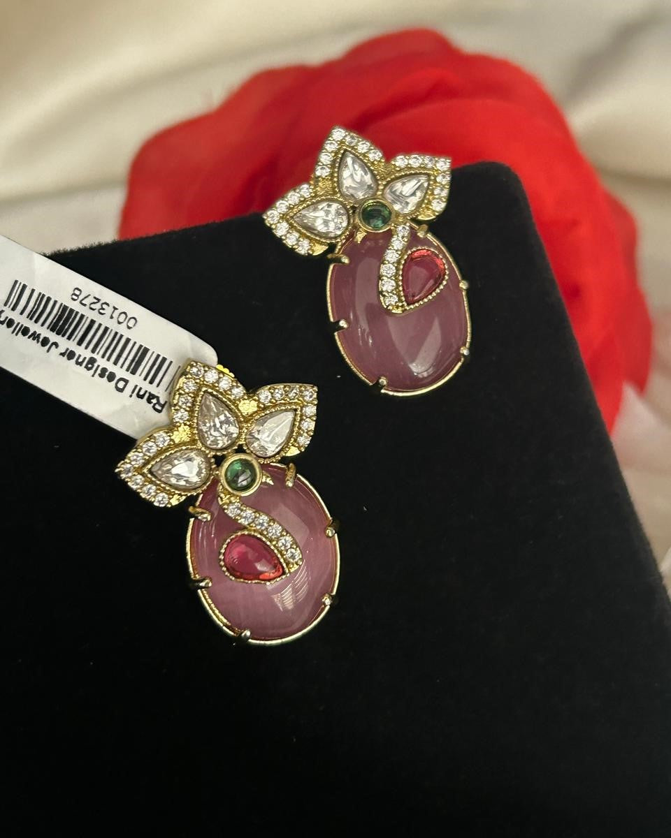 Pair of ornate earrings with gemstones on a black stand with a red cloth background