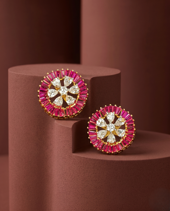 Pair of ornate earrings with pink and gold accents on a brown cylindrical stand.