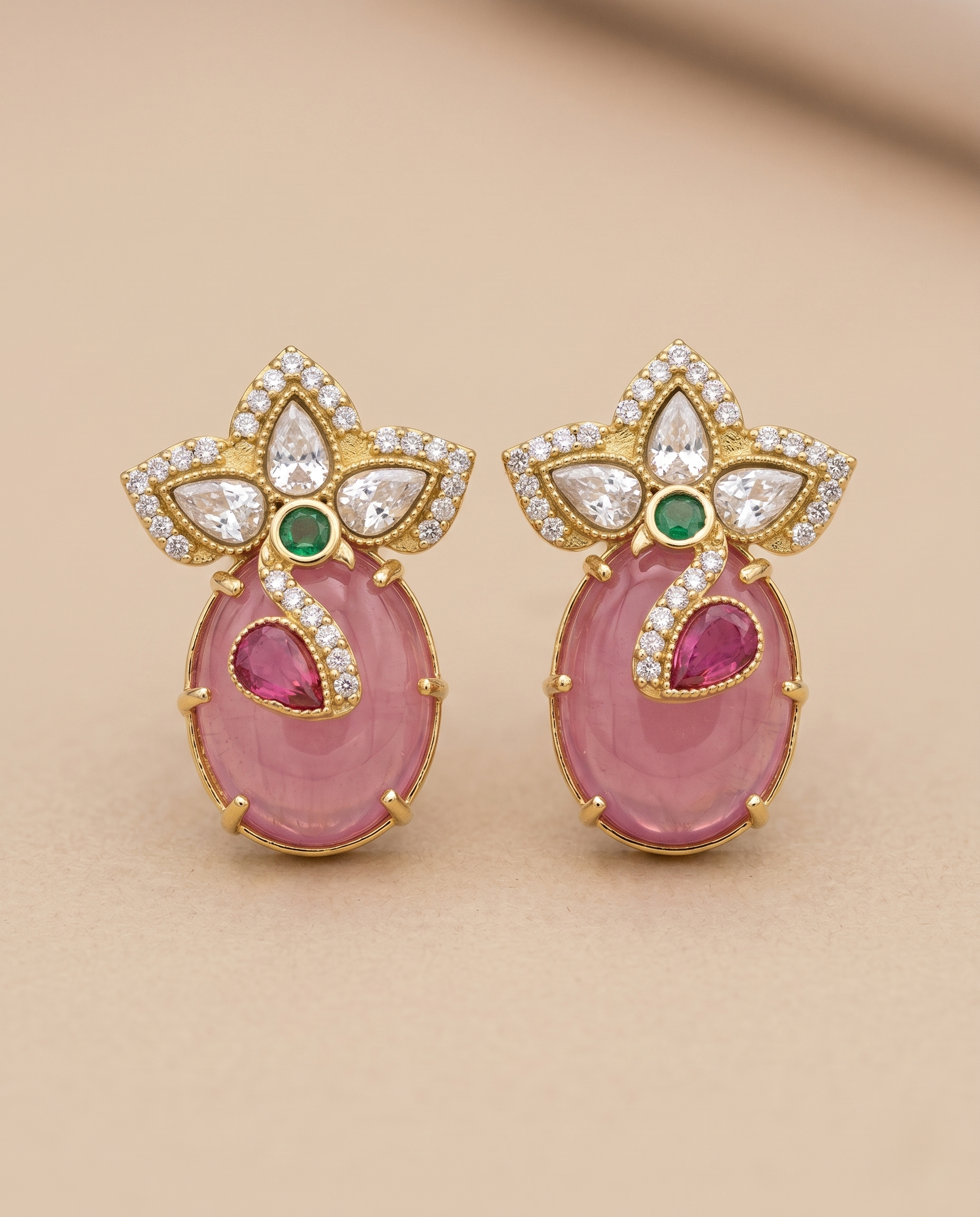 Pair of ornate earrings with pink stones and gold accents on a beige background