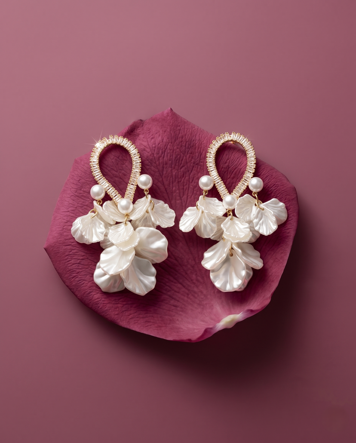Pair of pearl earrings on a pink petal against a purple background