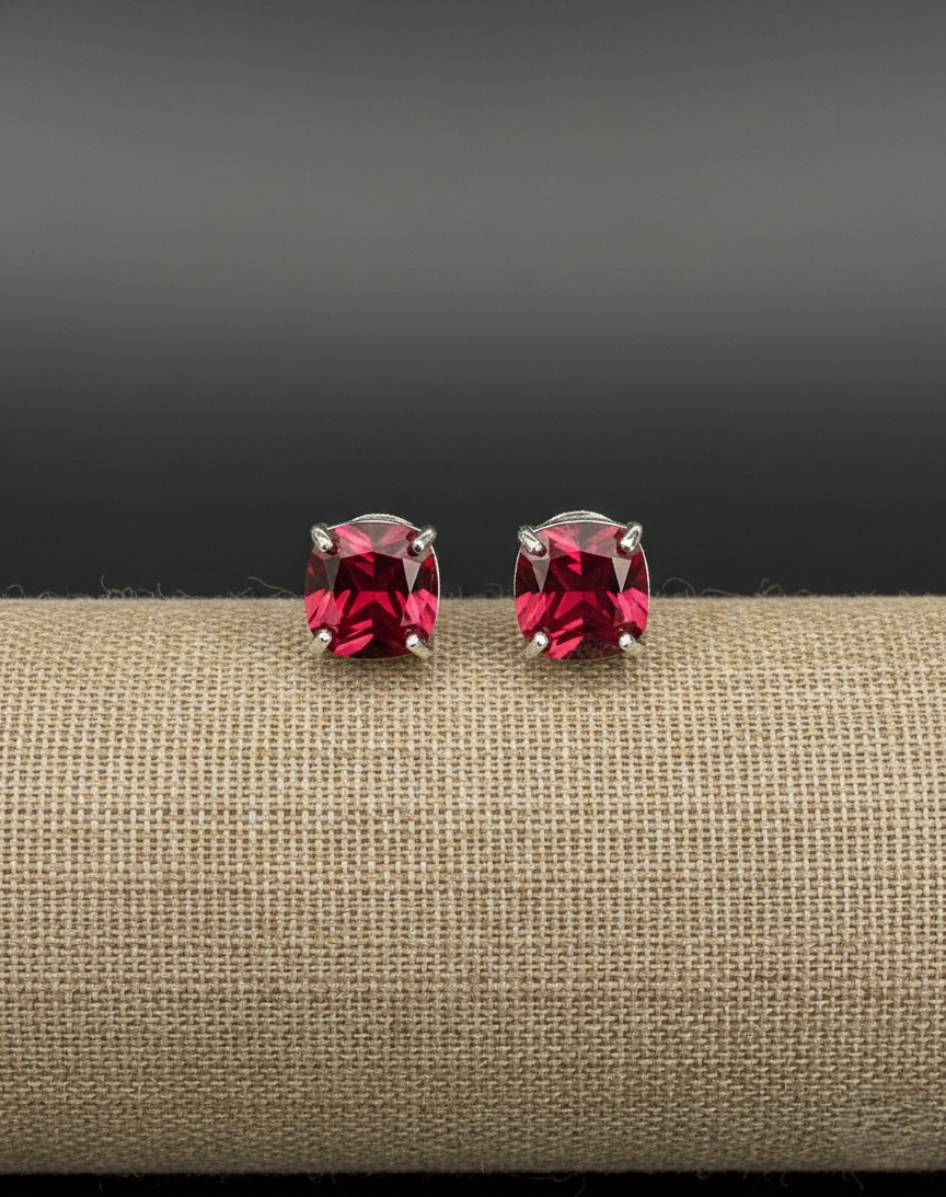 Pair of red gemstone stud earrings on a beige surface with a dark background