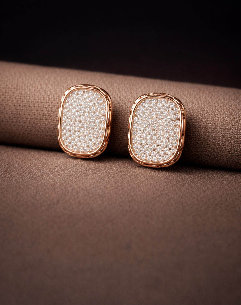 Pair of rose gold earrings with clear gemstones on a brown fabric background