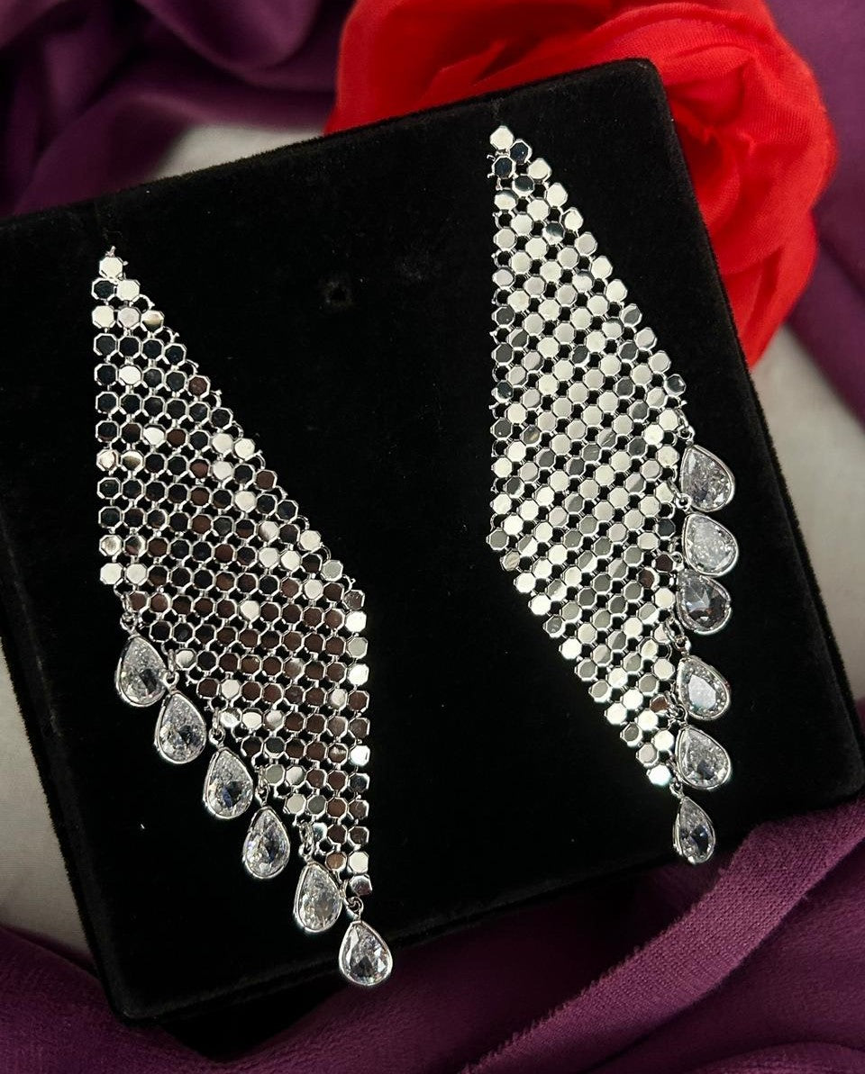 Pair of silver earrings on a black velvet stand with a red fabric background