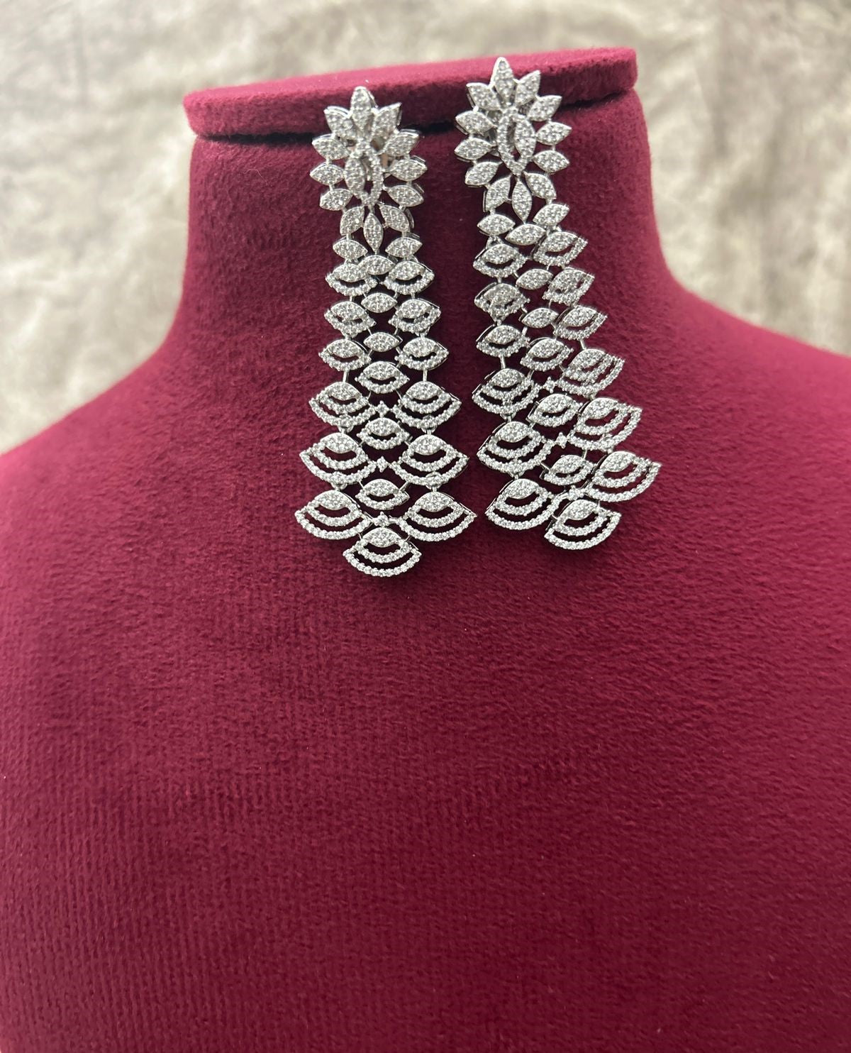 Pair of silver leaf-shaped earrings on a mannequin with a textured background
