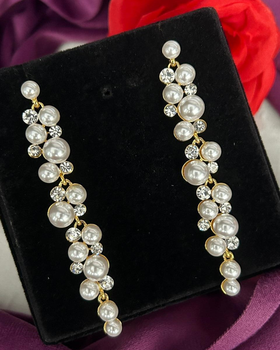 Pearl and crystal earrings on a black velvet stand with a red flower in the background.