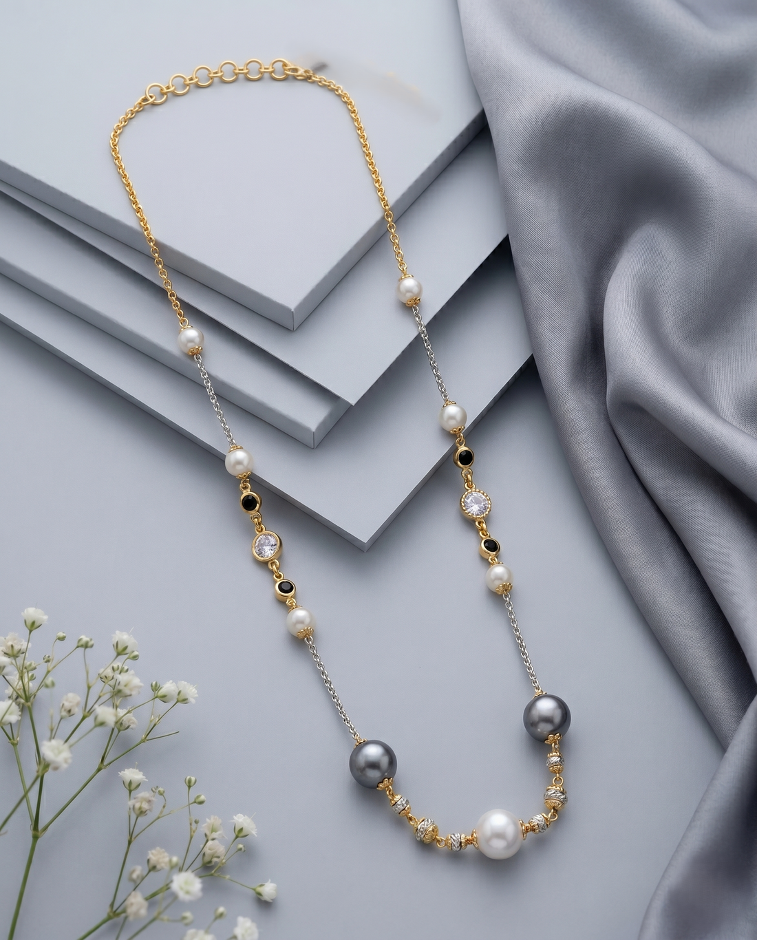 Pearl necklace with gold and silver accents on a gray fabric background