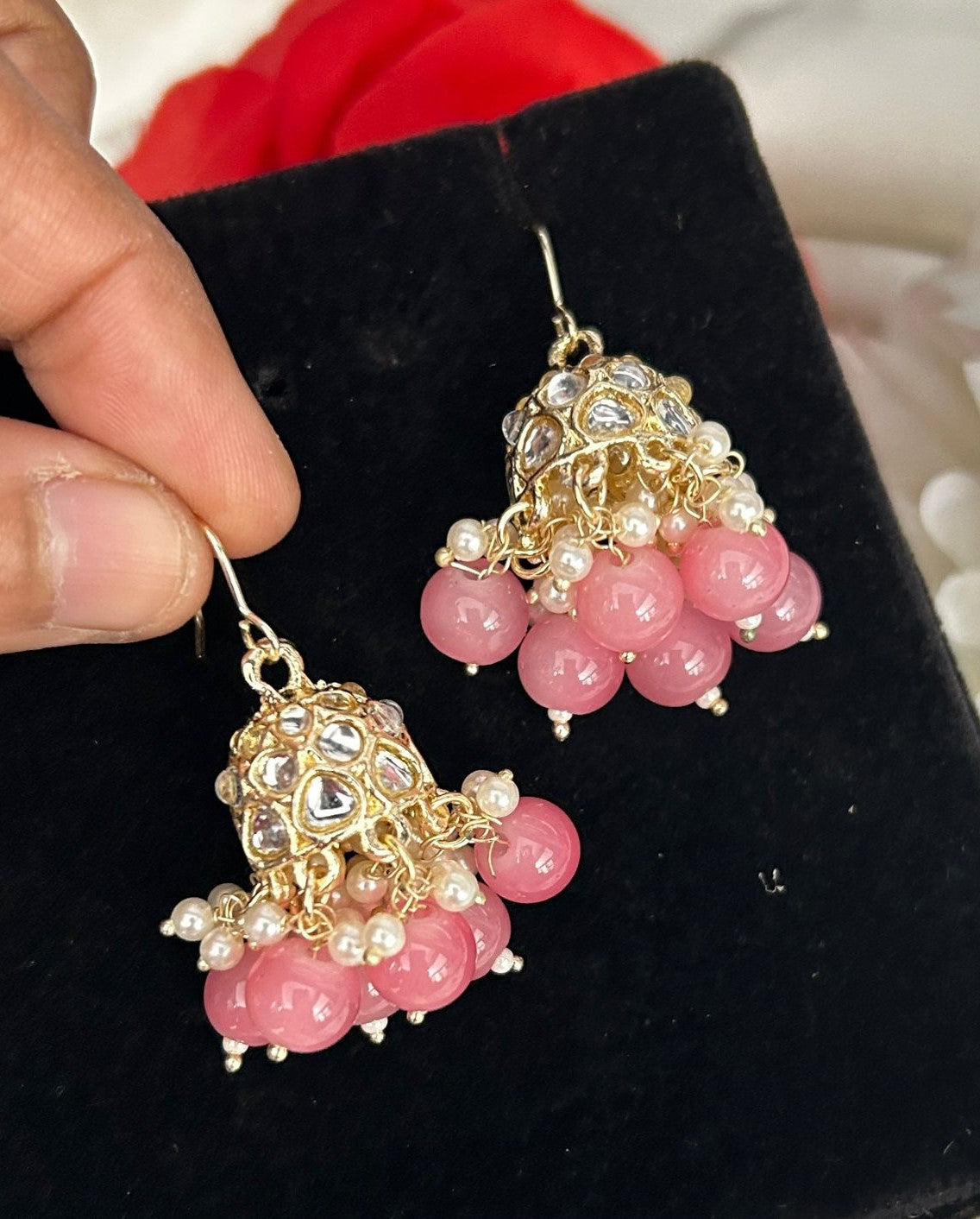 Pink beaded earrings with gold accents held by a hand on a black background