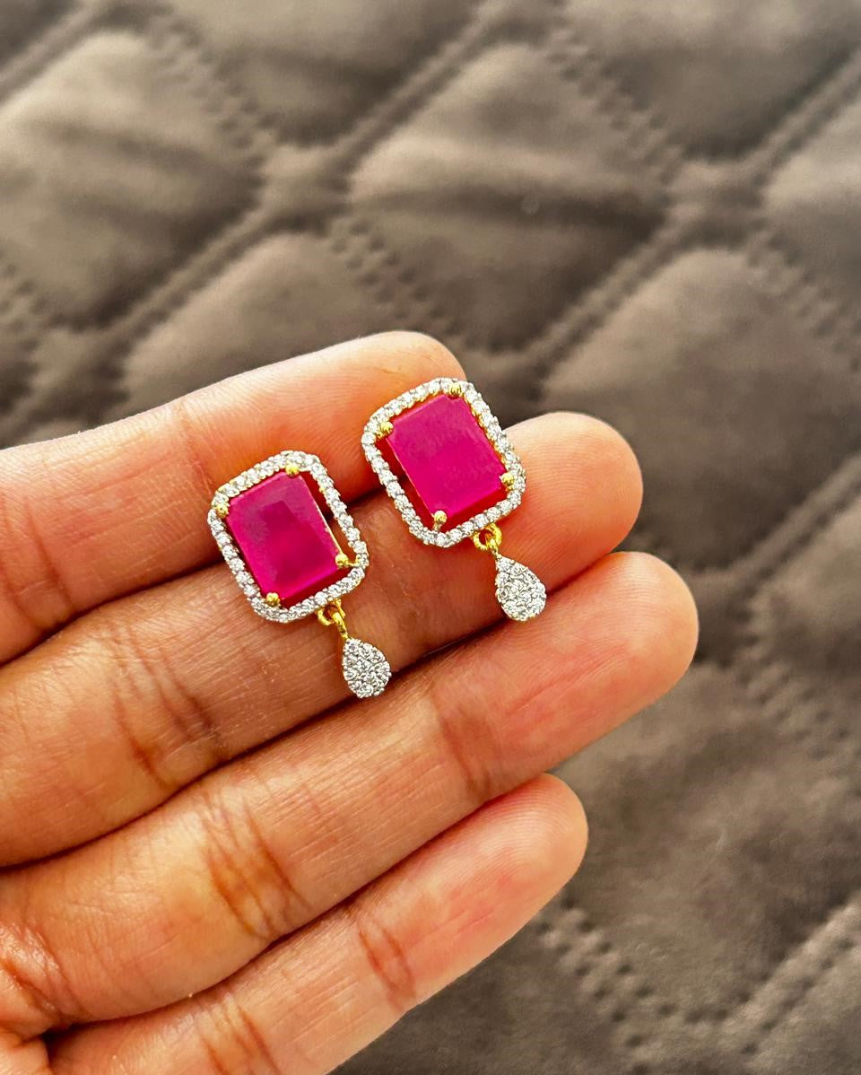 Pink gemstone earrings with gold and silver accents held in a hand against a textured gray background.
