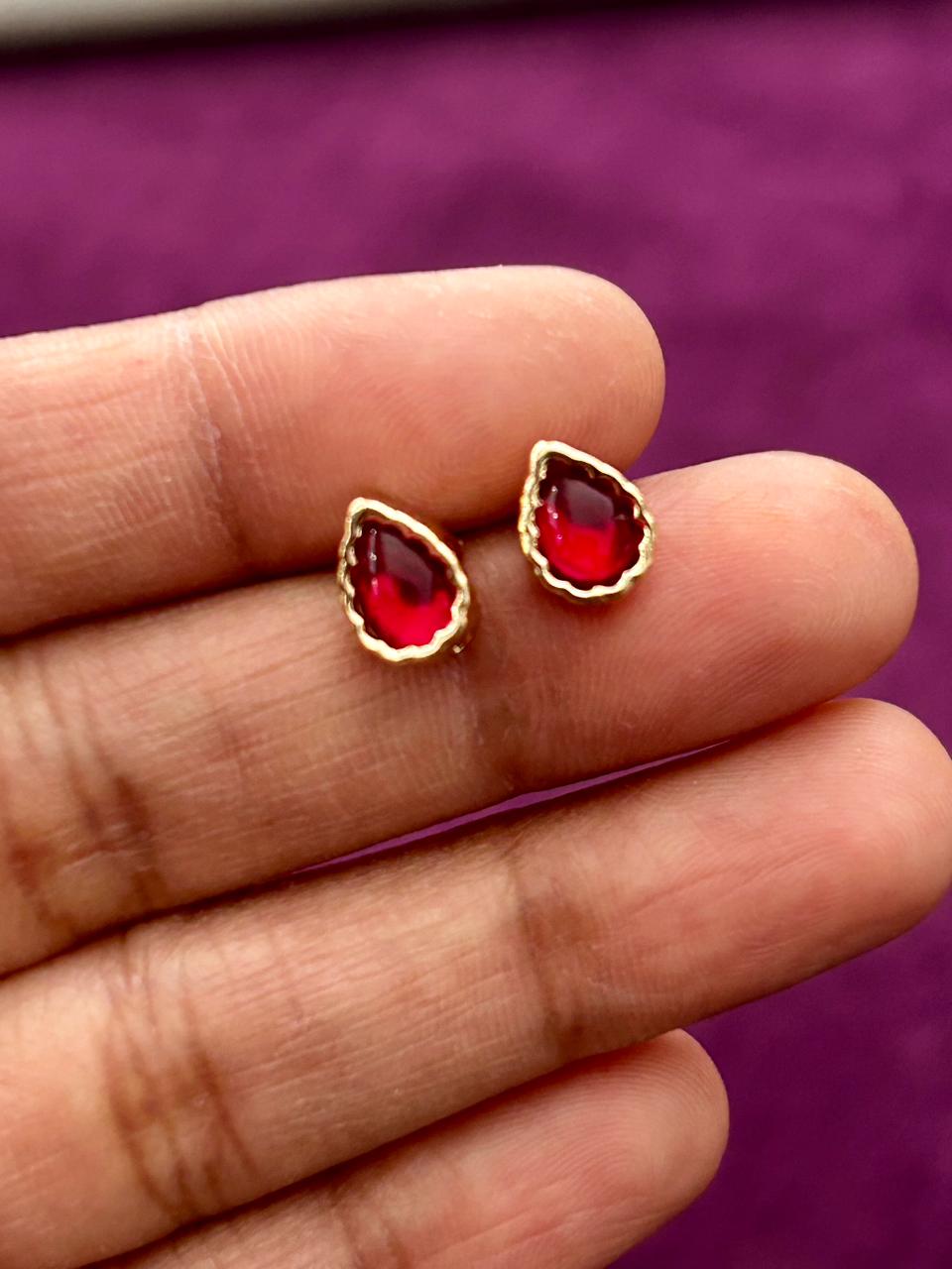 Red gemstone earrings with gold accents held between fingers against a purple background