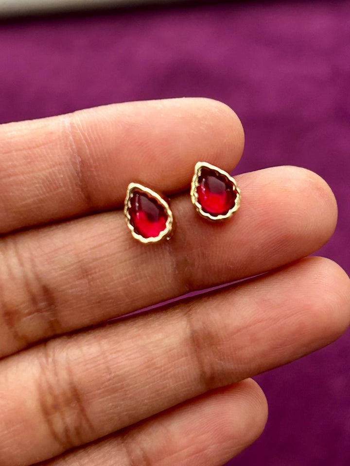 Red gemstone earrings with gold accents held between fingers against a purple background