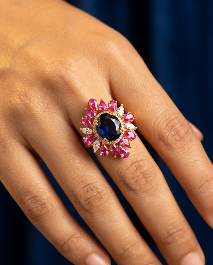 Ring with pink and blue gemstones on a hand against a dark background