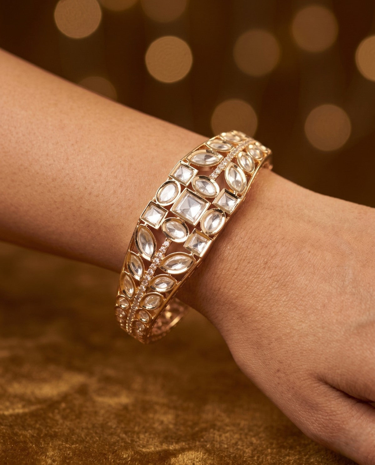 Rose gold bracelet with gemstones on a wrist against a warm brown background