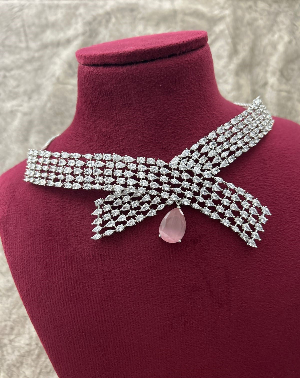 Silver bow-shaped necklace with a pink gemstone on a mannequin bust.