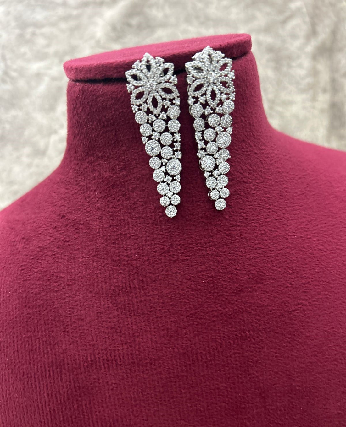 Silver earrings on a mannequin with a textured background