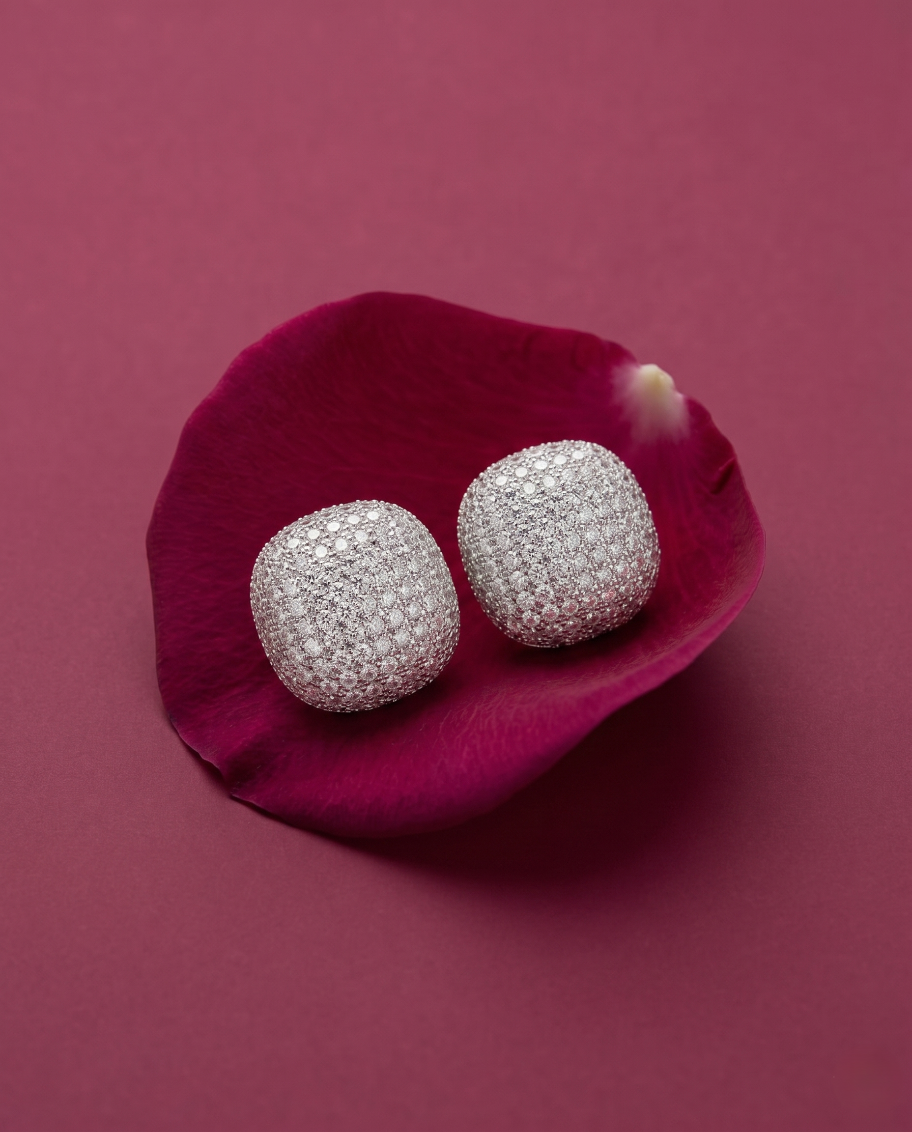 Silver earrings on a pink flower petal against a pink background