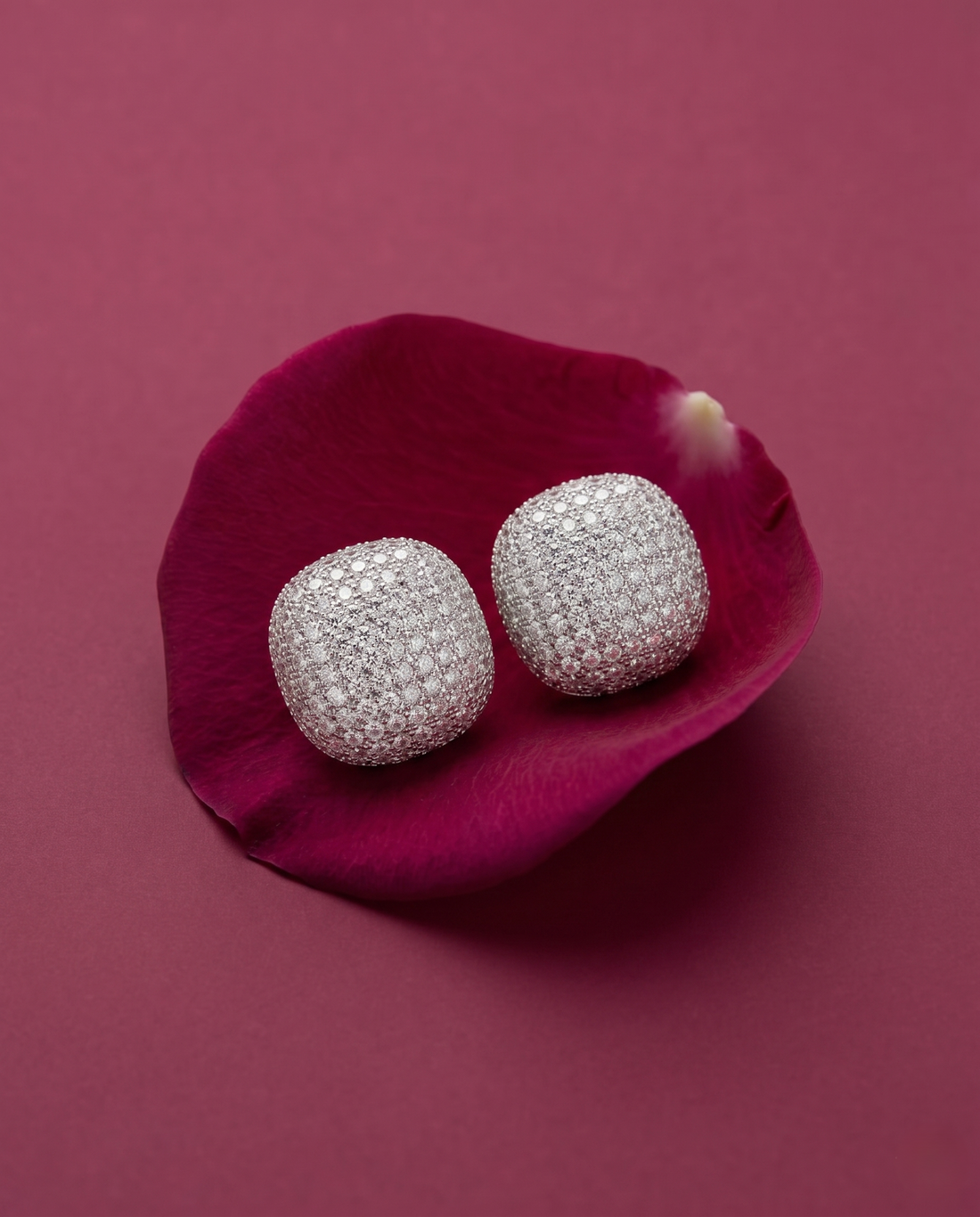 Silver earrings on a pink flower petal against a pink background