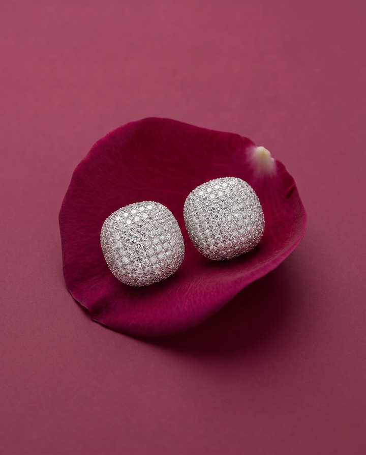 Silver earrings on a pink flower petal against a pink background