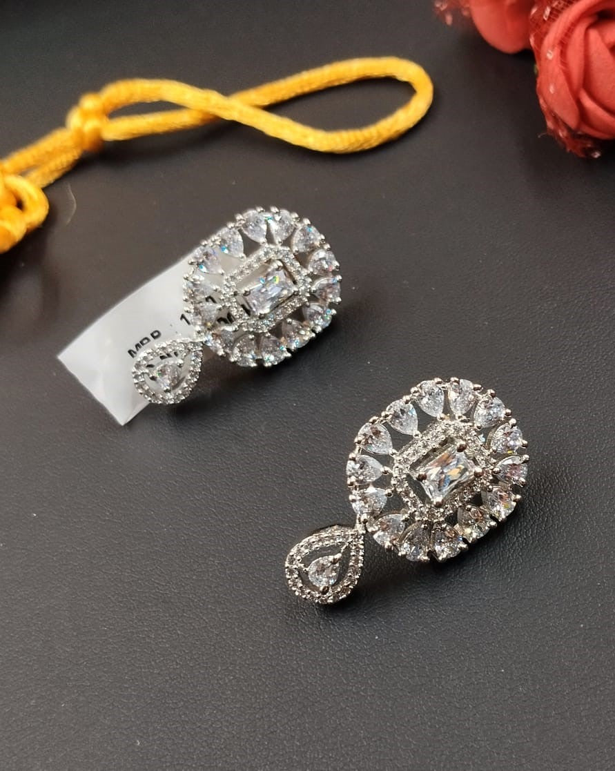 Silver earrings with clear gemstones on a dark surface