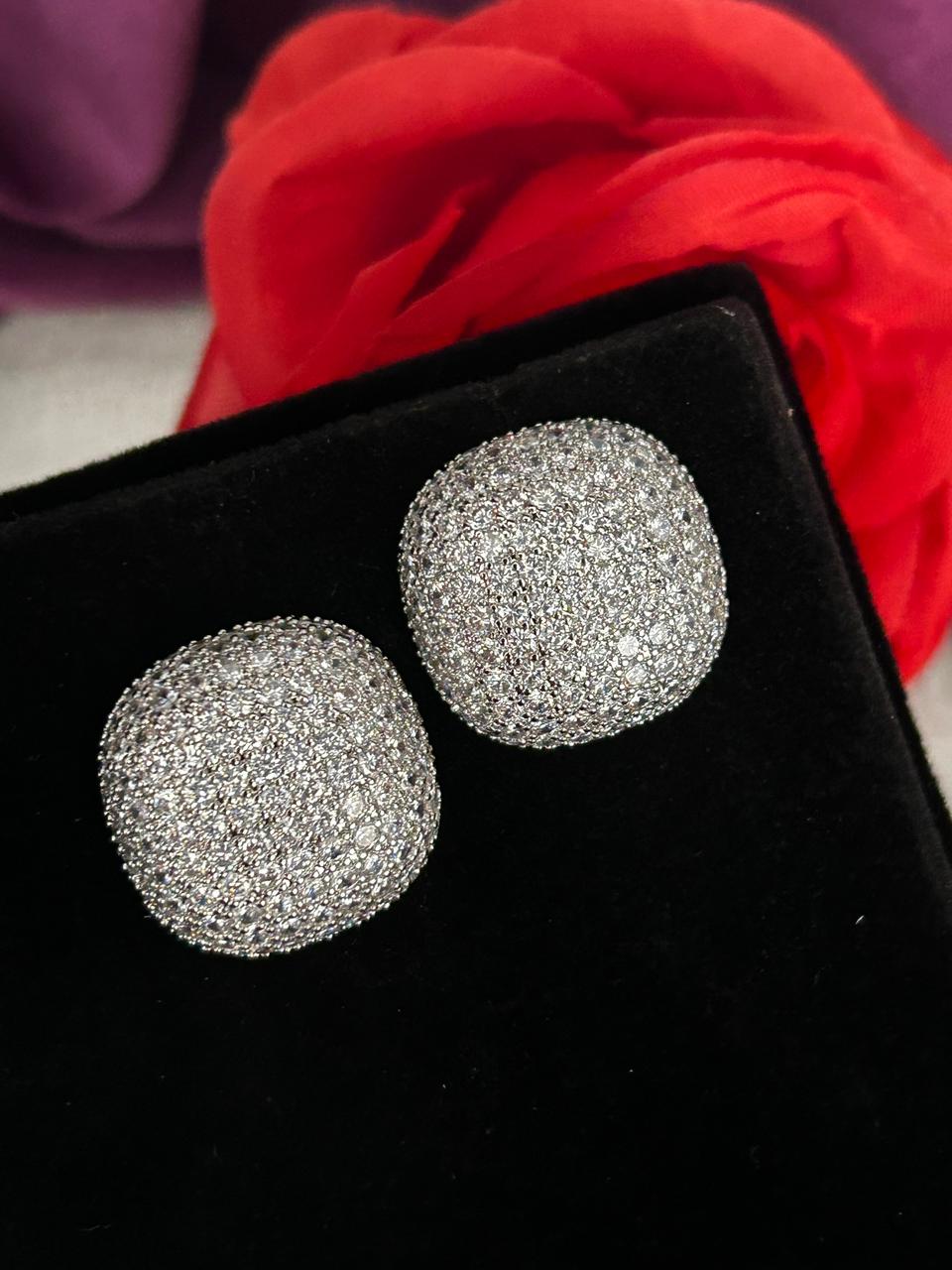 Silver glittery round earrings on a black box with red fabric in the background