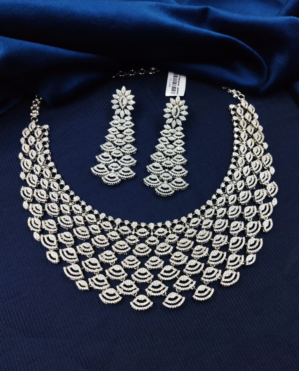 Silver necklace and earrings set on a dark blue fabric background