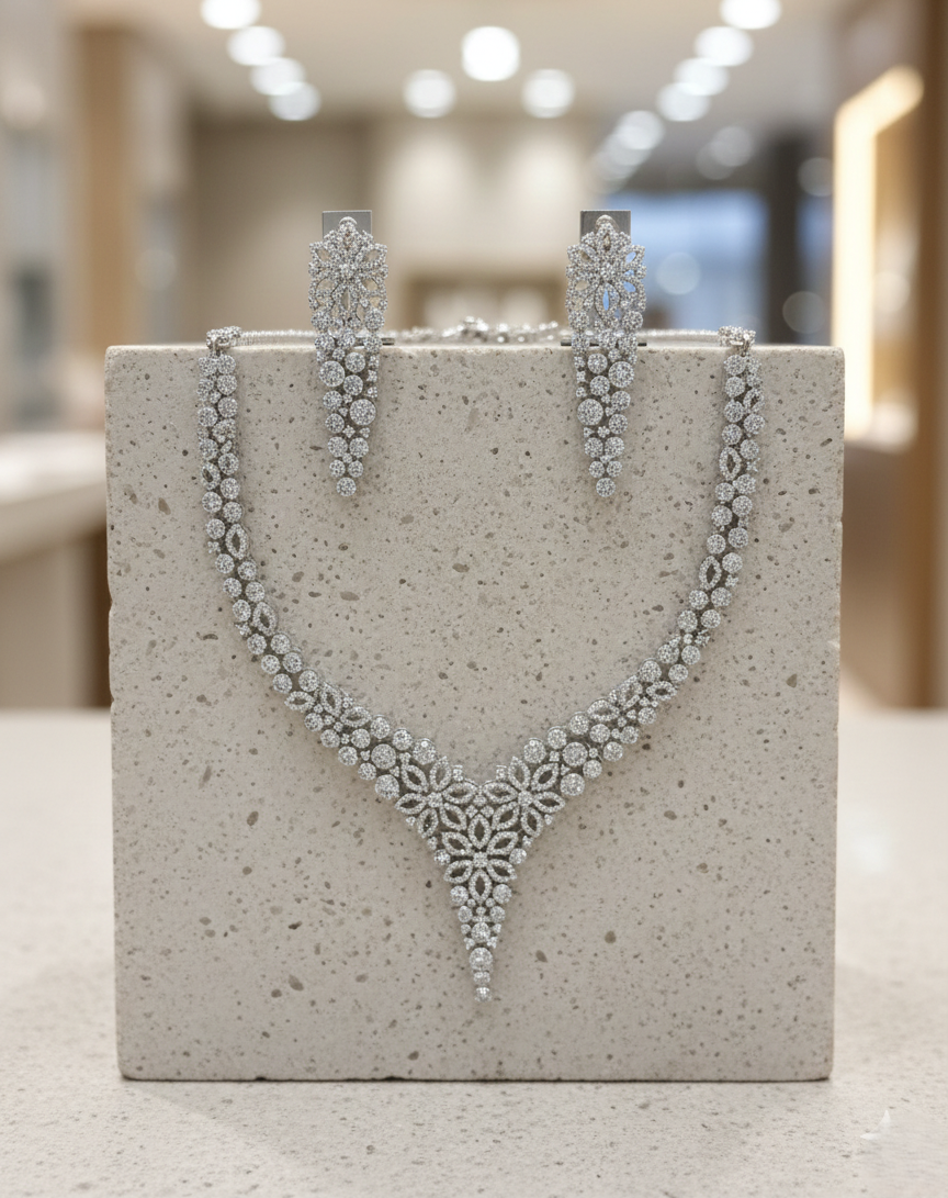 Silver necklace and earrings on a textured gray stand with a blurred indoor background