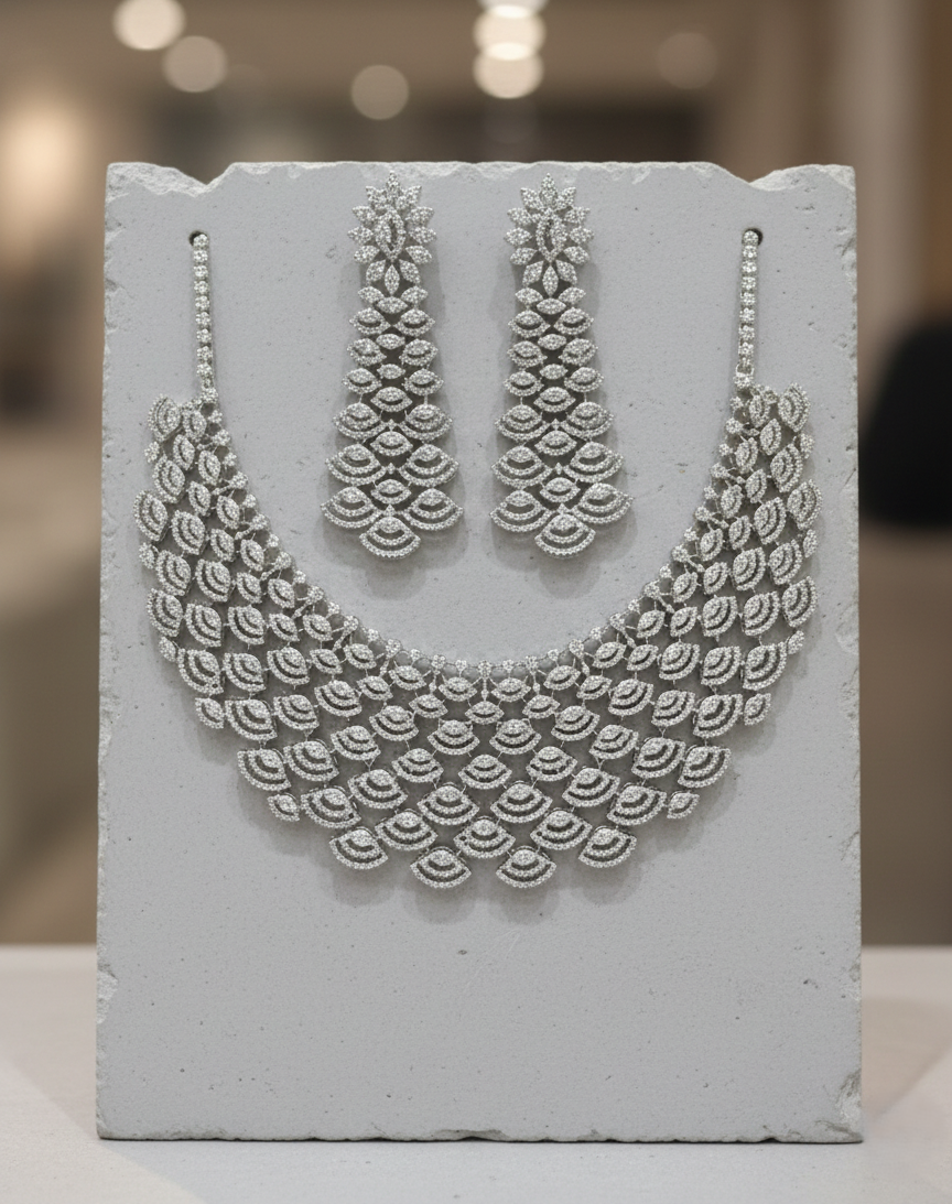 Silver necklace and earrings set on a textured white surface with a blurred background